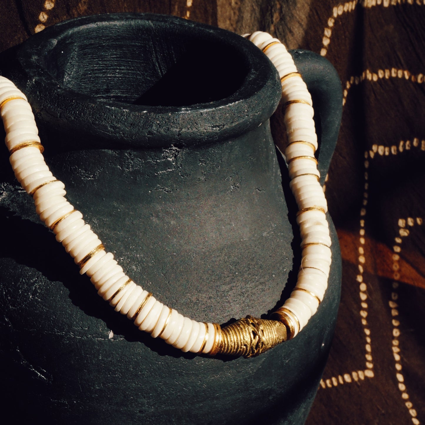shell necklace with gold spacers and a brass pendant hanging from a black ceramic pot