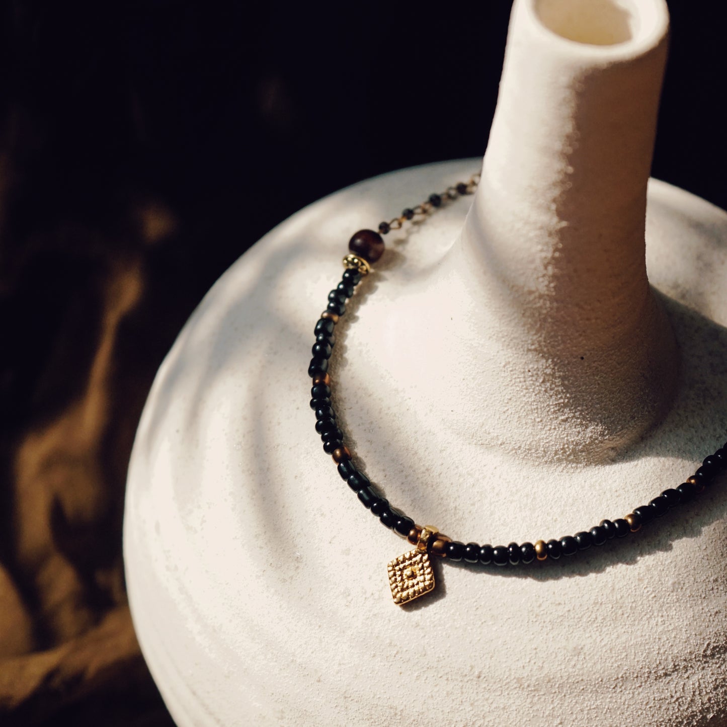 Beaded and Brass Necklace draped over a white ceramic pot