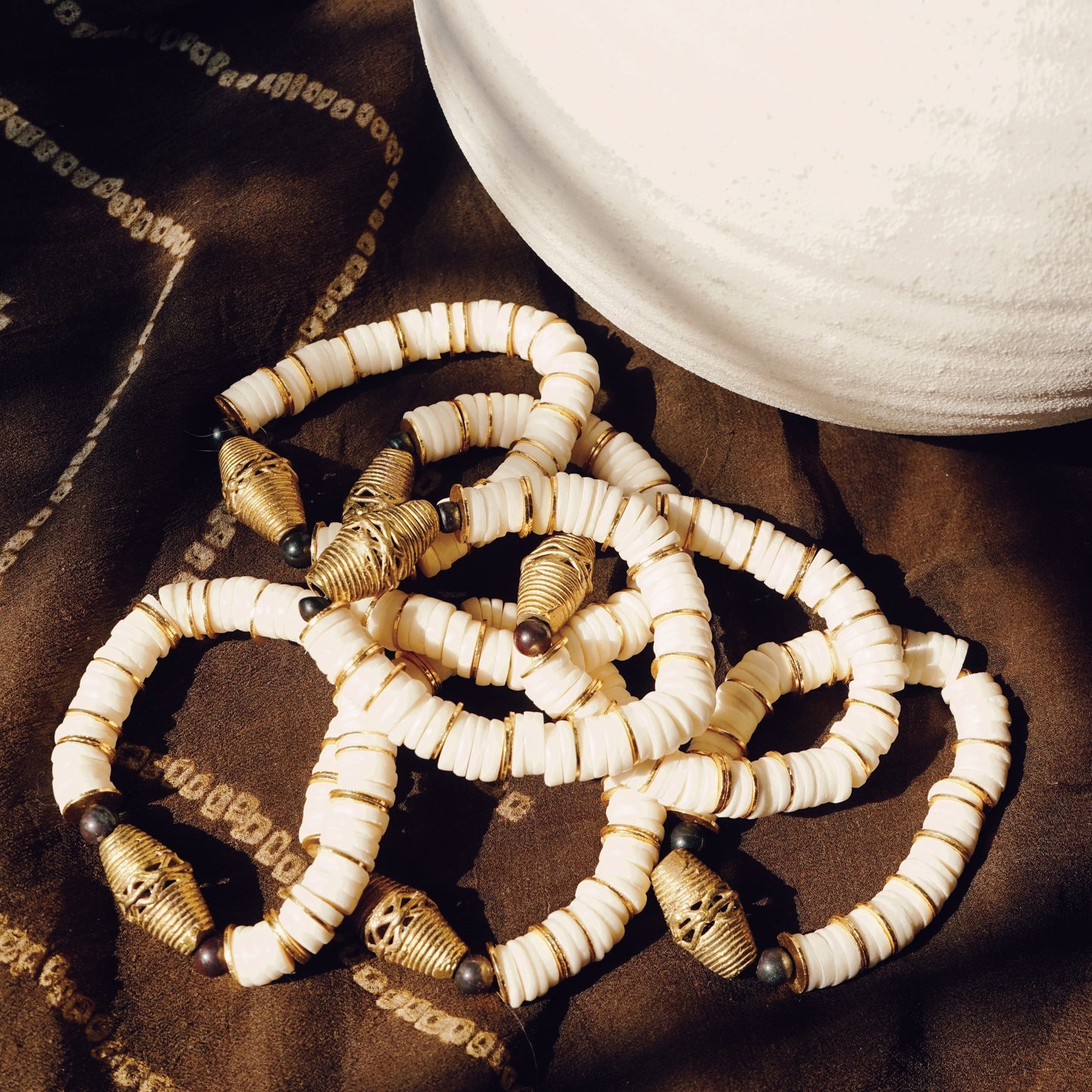 Multiple pearl shelled bracelets with gold pendants stacked on top of each other